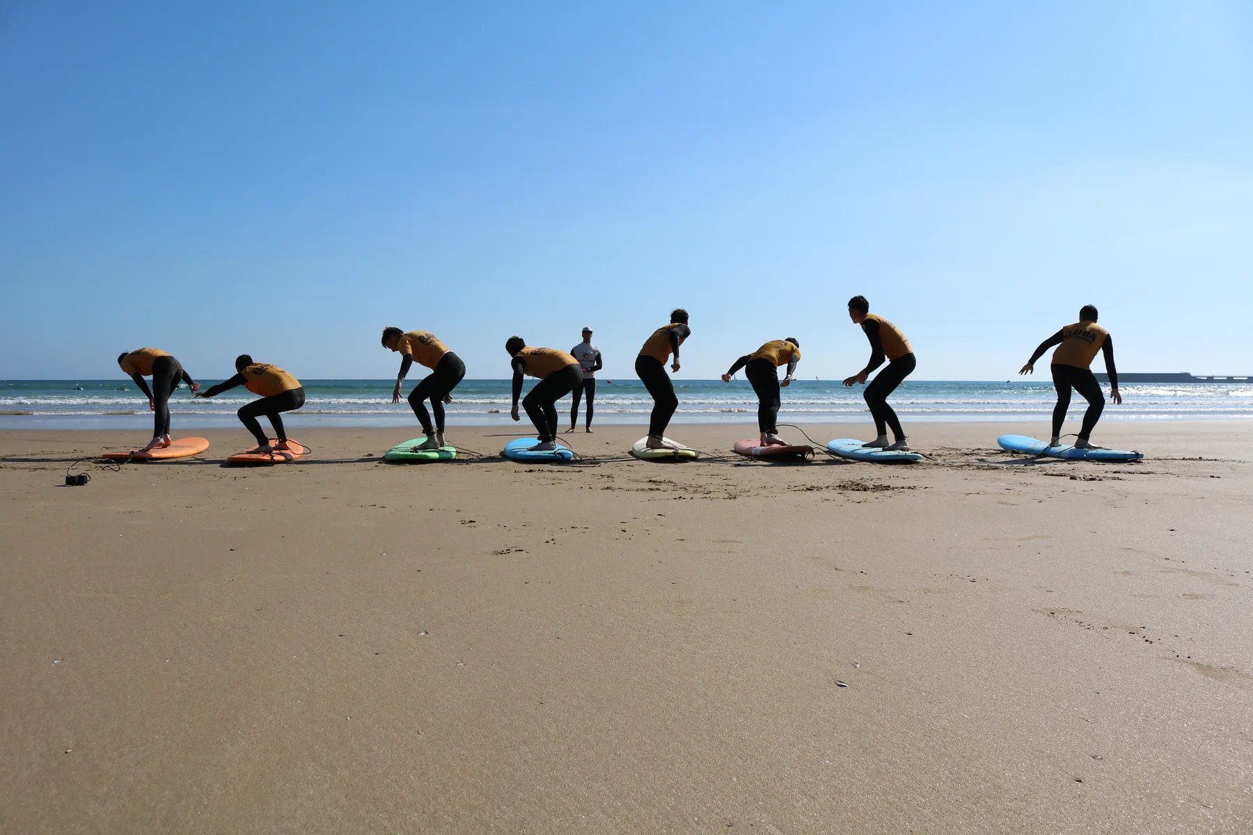Les mêmes élèves, cette fois en train de se redresser debout sur leurs planches posées sur le sable.