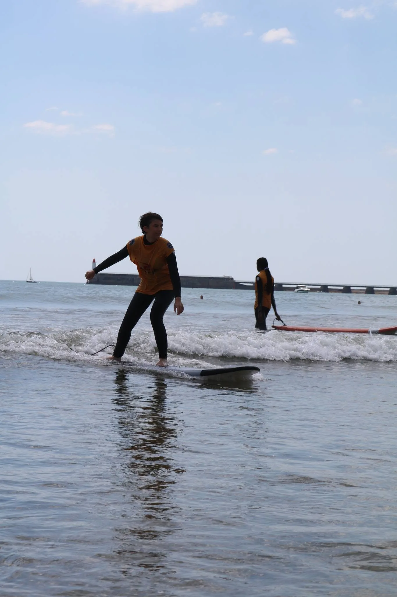 Un élève debout sur sa planche dans la mousse, bras écartés.