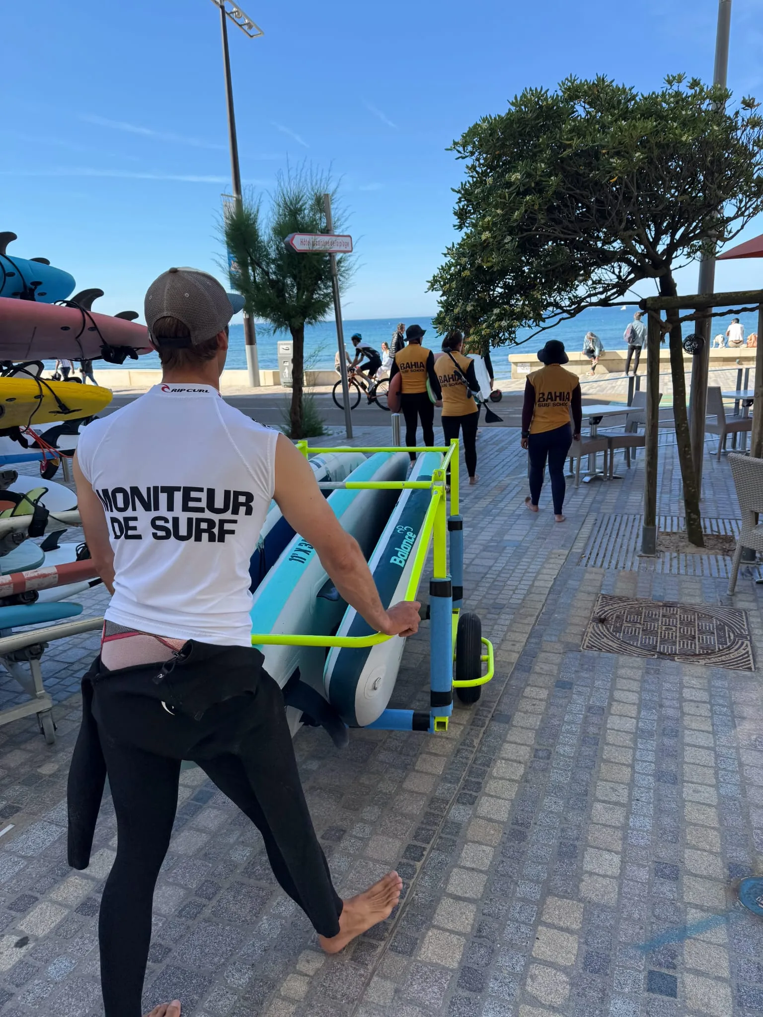 Le moniteur pousse le chariot de planches sur la promenade, devant le magasin.