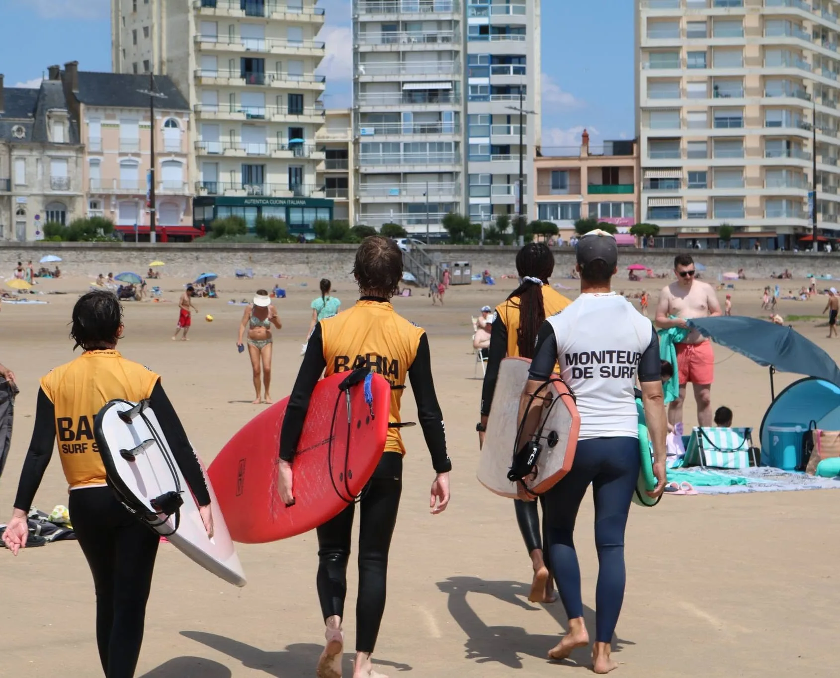 Le groupe remonte la plage, planches sous le bras, devant le front de mer des Sables.