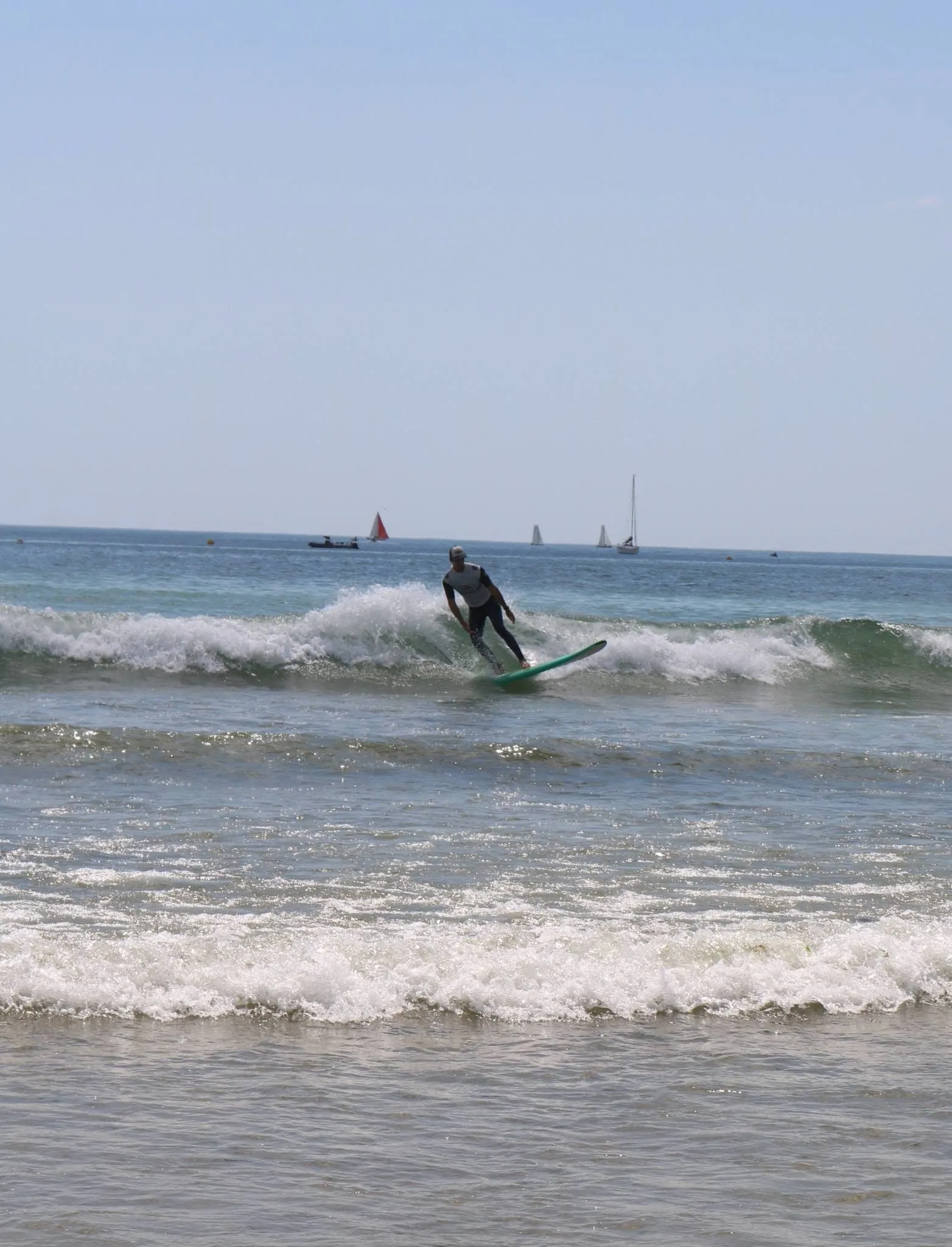 Un surfeur debout sur une petite vague verte.
