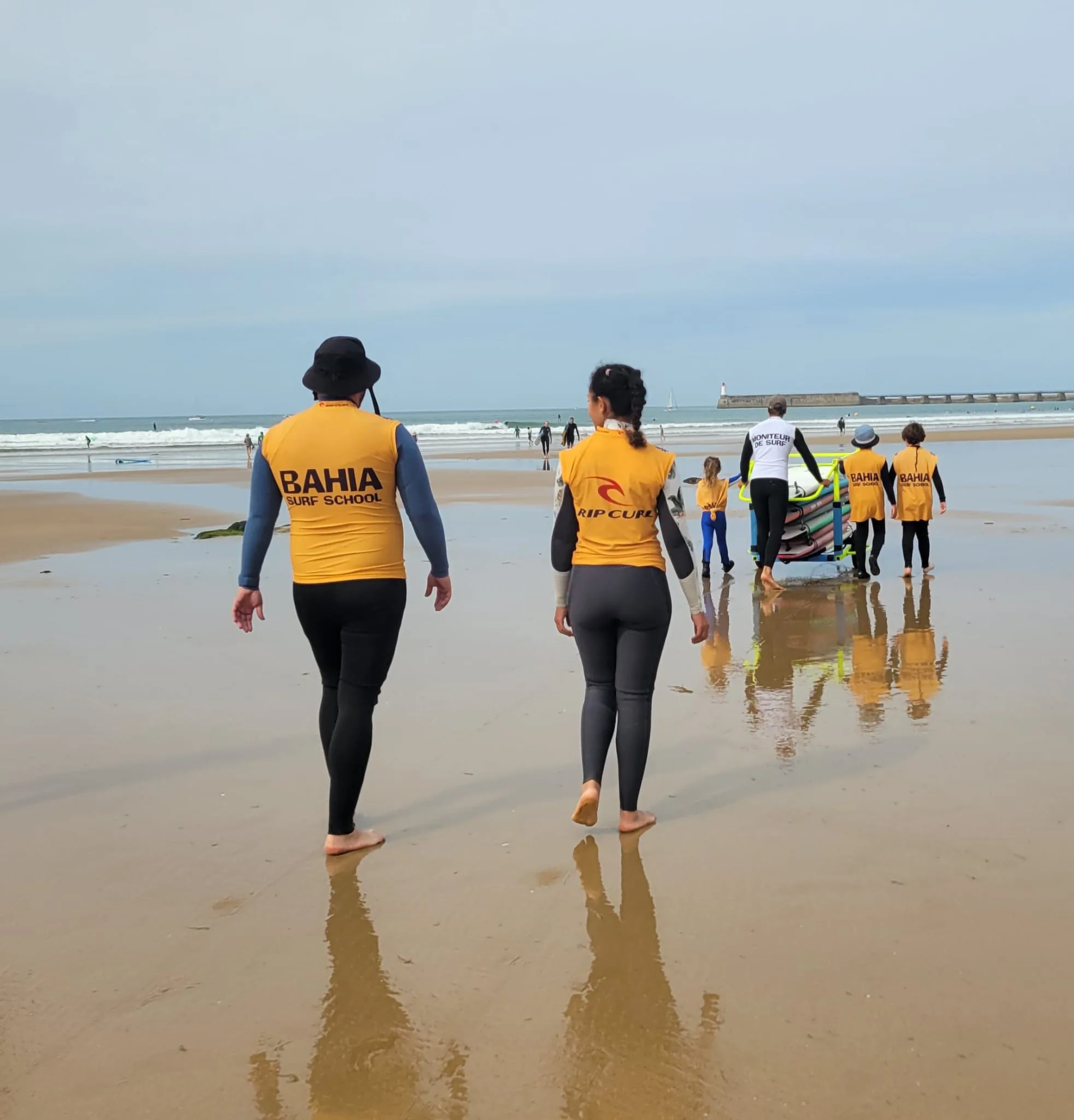 Deux élèves de dos marchent vers l’eau sur le sable mouillé.