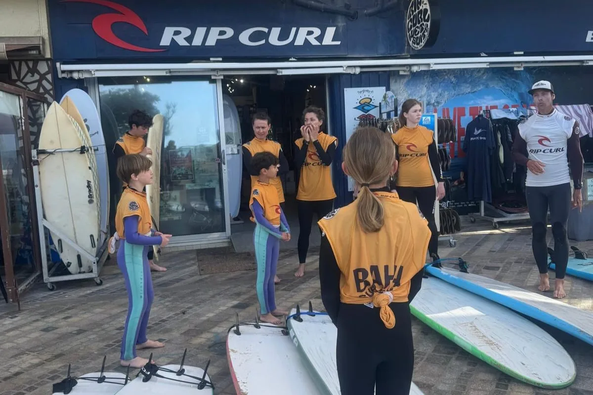 Le groupe en lycra Bahia rassemblé devant le magasin Bahia Surf Shop, les planches posées au sol avant de descendre à la plage.