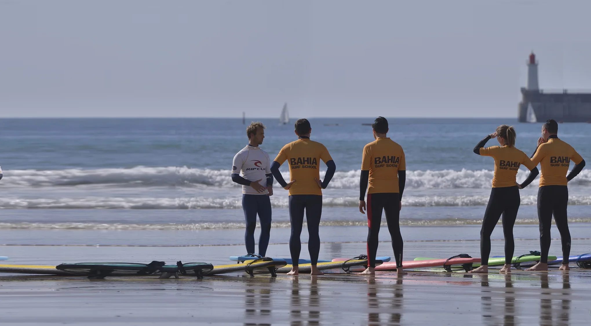 Le groupe face à la mer sur le sable mouillé, la grande jetée et le phare rouge au fond.