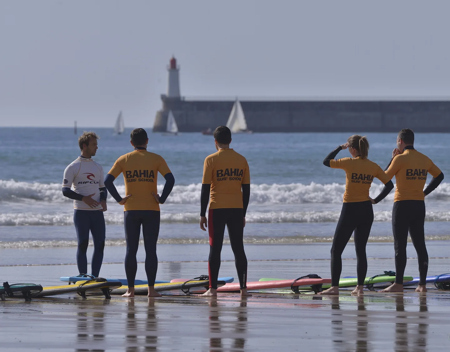 Le groupe face à la mer sur le sable mouillé, la grande jetée et le phare rouge au fond.